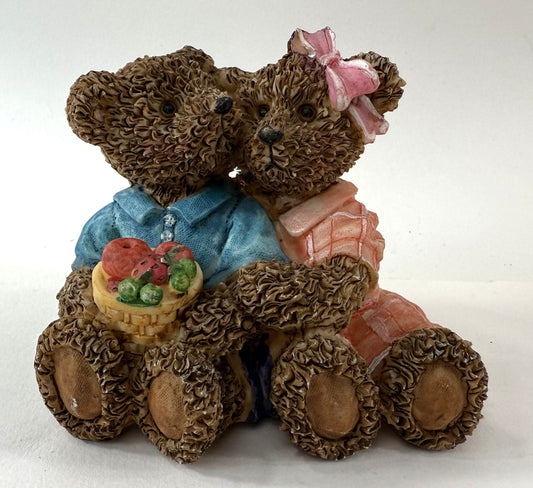 Two teddy bears sitting together with a basket of fruit